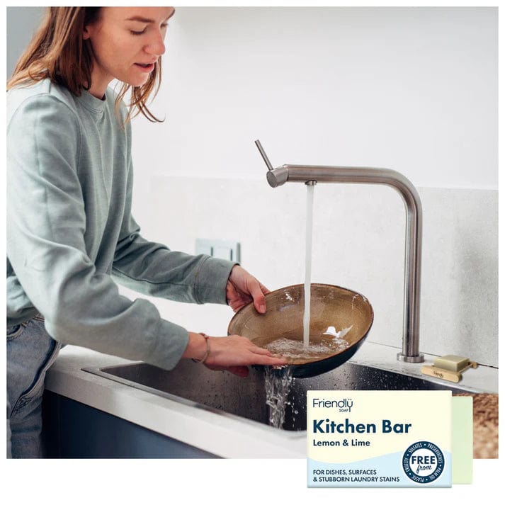 Person washing dishes with eco-friendly Kitchen Bar Lemon & Lime, promoting biodegradable dish soap.