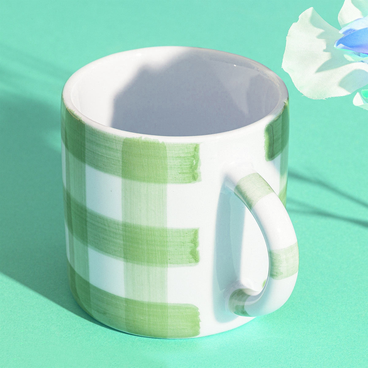 Green gingham-inspired stoneware mug with green and white checkered pattern, featuring a handle, on a green background. Dishwasher and microwave safe.